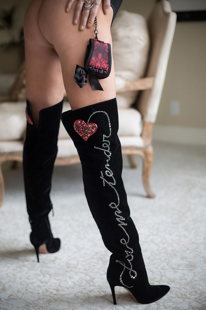 A close-up of a woman's thigh in thigh-high black boots with decorative elements and a small pouch on the leg.